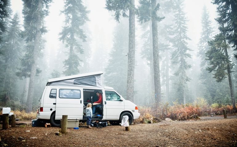 Father sitting in camper van in discussion with young daughter at campsite in woods