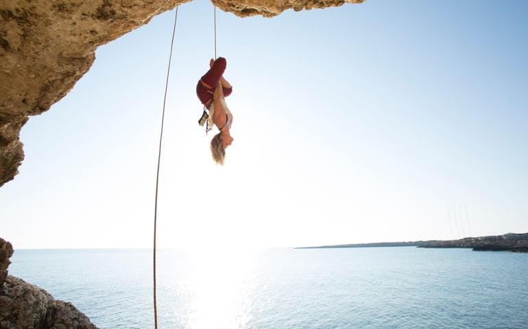 Young woman hangs from rope, vertical yoga stance
