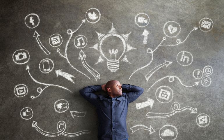 Confident African man relaxes inside a universe of chalkboard social media, music, communications, tech symbols