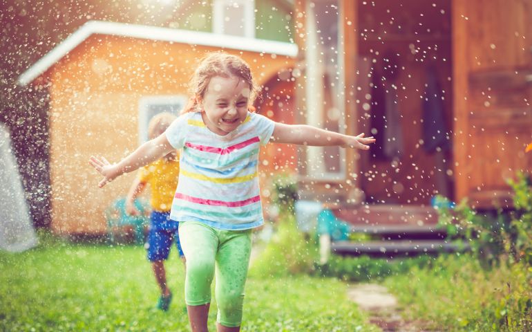 Happy children playing with garden sprinkler in summer