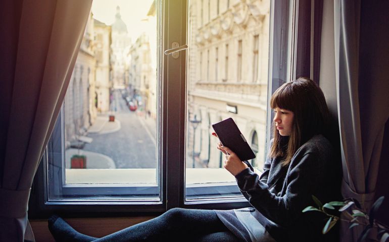 Young teenage girl is reading ebook on the window with very nice city view