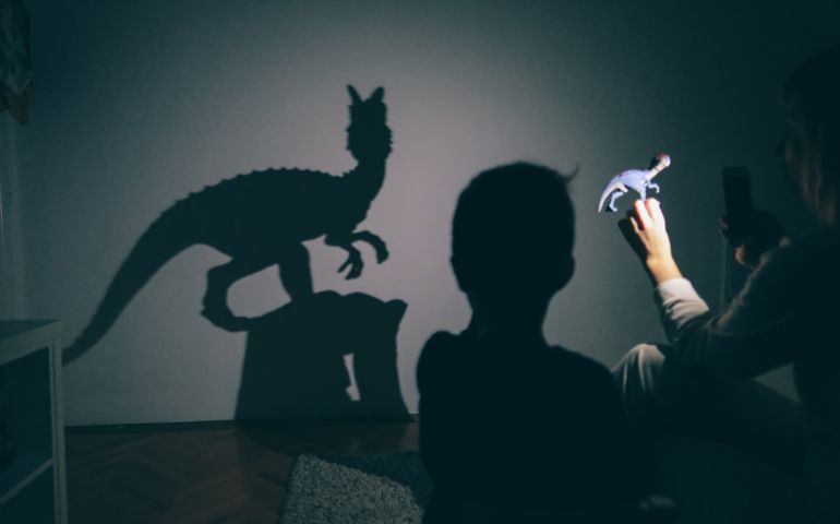 Little boy and his mother are playing with shadow puppets on the wall by using dinosaur toys