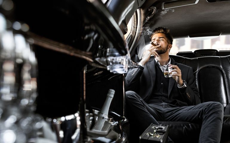 Pensive businessman in a limousine with glass of champagne smoking cigar looking through window
