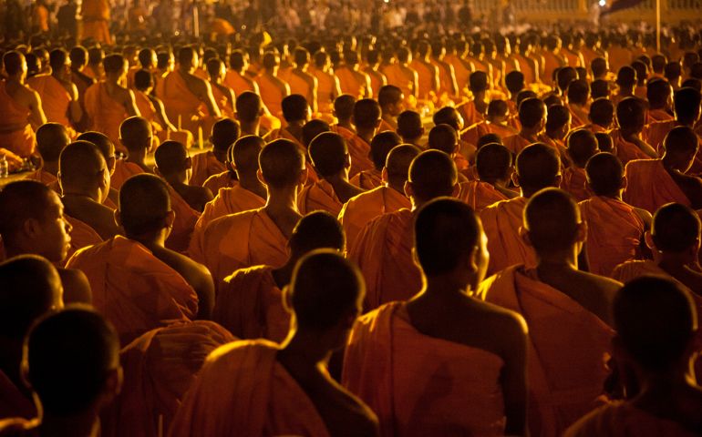 Thousands of monks sit in robes illuminated by the light of Royal Palace