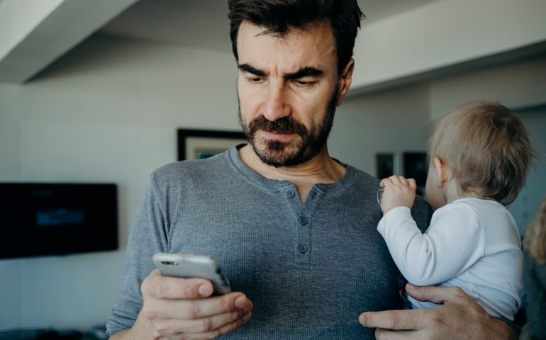 Father holding baby reading phone