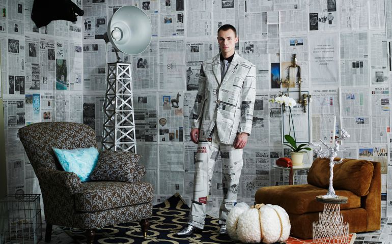 Man standing in room filled with recycled items and newspaper walls