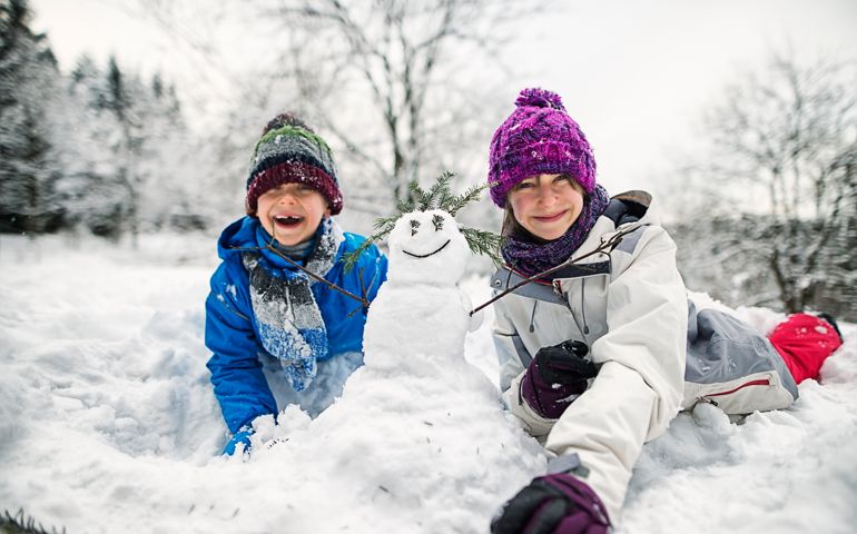 Cold winter day. Little boy and little girl went outside to play with snow. They are building a small cute snowman. Kids are aged 11 and 7.