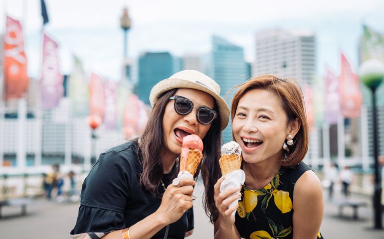 Cheerful Chinese mature women enjoying ice cream in Sydney, in summer. Two friends are traveling across Australia and having fun together