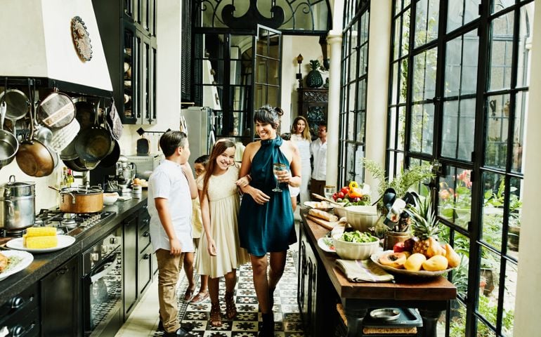Smiling aunt and niece walking through kitchen arm in arm during family dinner party