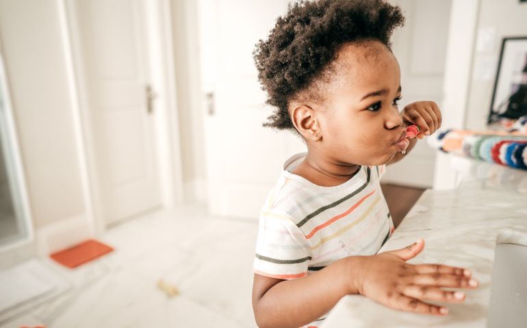 A baby girl brushing her teeth in front of the mirror.