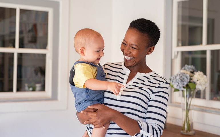 Portrait of happy black mother holding cute toddler laughing together at home.