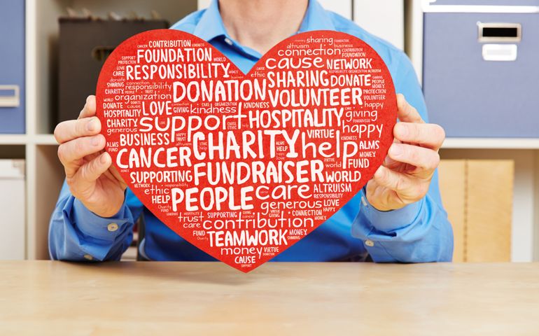 Man holding big red heart with charity and fundraiser tag cloud against cancer