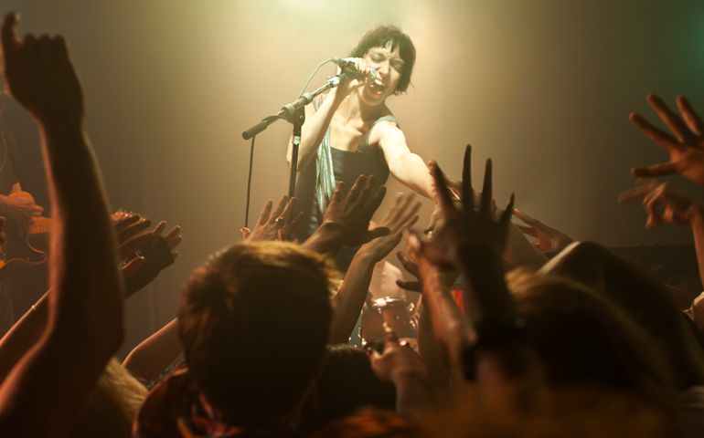 Rock band playing with woman singing into microphone while reaching towards the crowd of fans