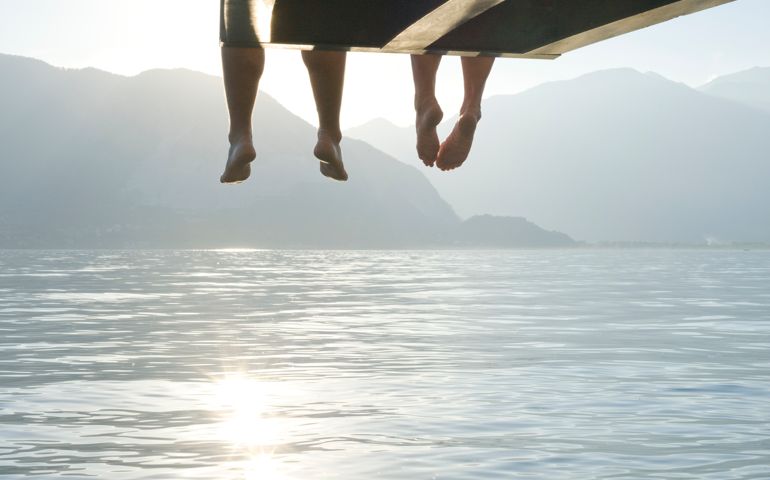 Couple's feet dangle from end of lake wharf