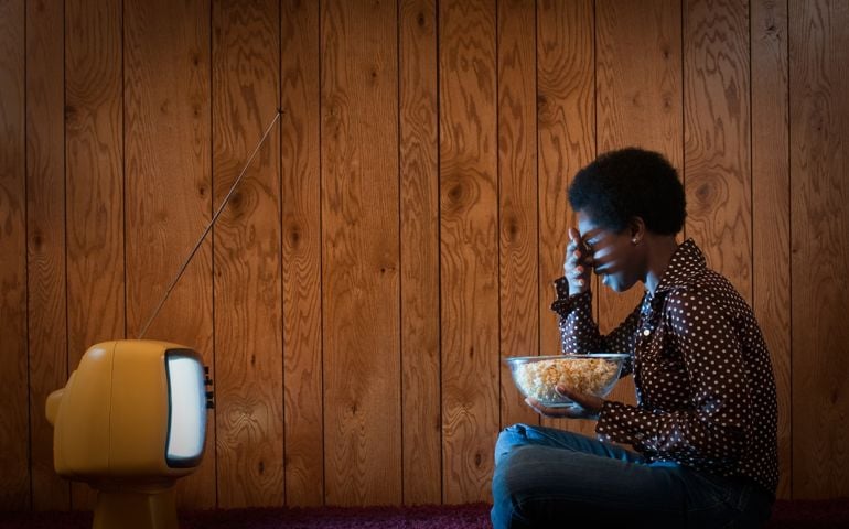 Woman shielding her eyes while watching vintage television, holding popcorn