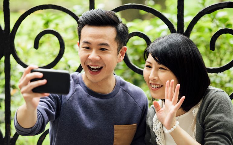 Mid adult couple smiling and taking photo of themselves, woman waving, weekend activities, social media, commuication