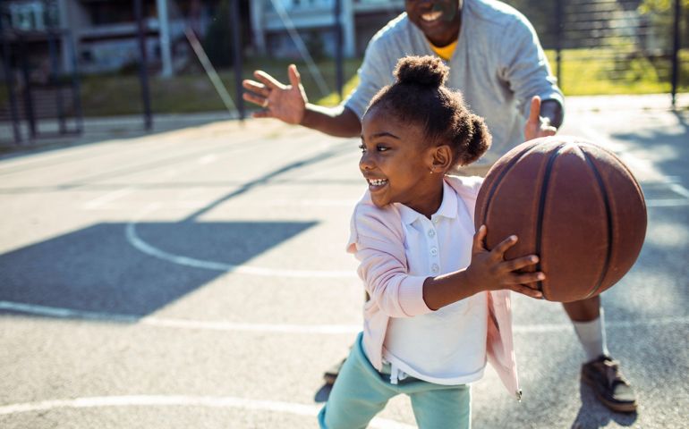Close up of a grandfather taking his granddaughter to play some basketball in the park