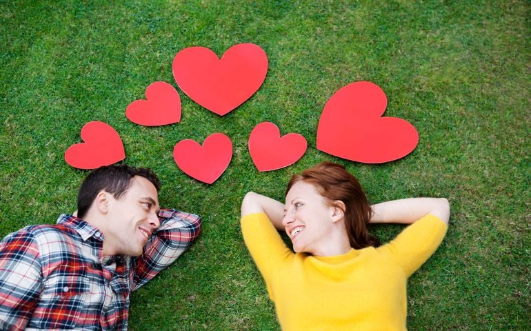 Couple laying in grass,surrounded by hearts.