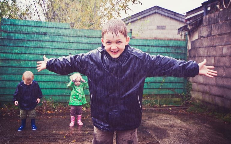 Smiling boy getting wet out in the rain with his arms stretched out.