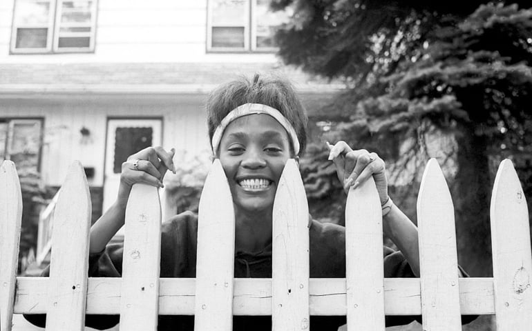 American singer and actress Whitney Houston (1963 - 2012) looks over the picket fence of her mother's home, West Orange, New Jersey, May 28, 1985.