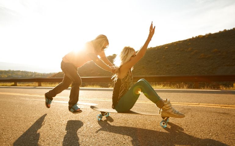 A guy pushing a girl on a skateboard.