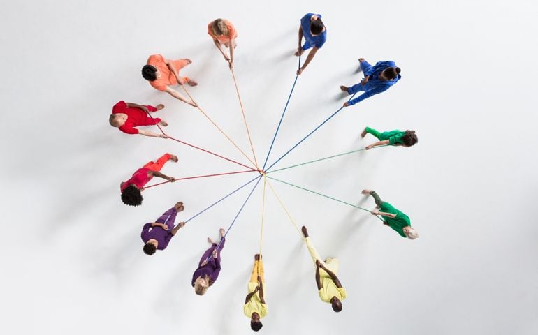 Overhead shot of a small group of people, wearing monochromatic colors, pulling at ropes from opposing directions