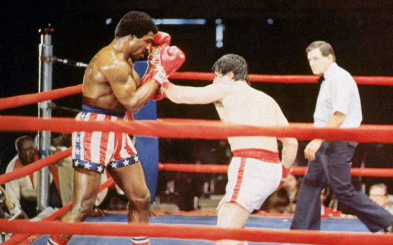 1976: American actor Sylvester Stallone, as Rocky Balboa, punches American actor Carl Weathers, as Apollo Creed, during a boxing match in a still from the film, 'Rocky,' directed by John G Avildson.