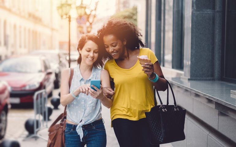 Smiling girls walking at the street and using smartphone