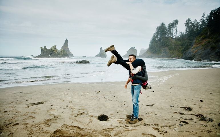 Man carrying girlfriend over shoulders on beach laughing