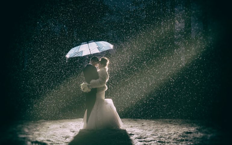 A couple stand in a snow storm under an umbrella during a blizzard