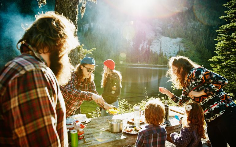 Group of friends and family dishing up dinner while camping near lake