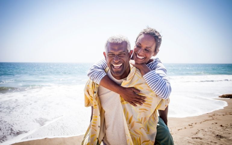 A beautiful senior black couple piggyback on the beach