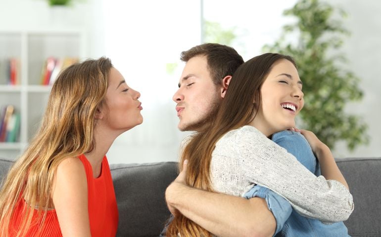 Boy cheating to his girlfriend with her best friend sitting on a couch at home