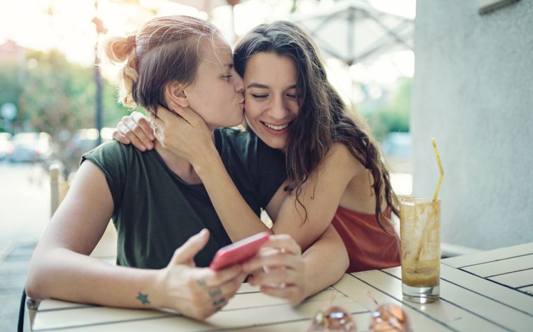 Young happy women drinking ice coffee outdoors on a hot summer day, embracing, kissing and having fun