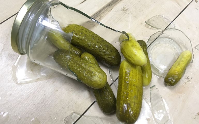 Accidentally broken jar of pickled cucumbers on a kitchen floor.