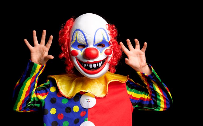 boy wearing clown mask, with hands in the air threatening onlookers