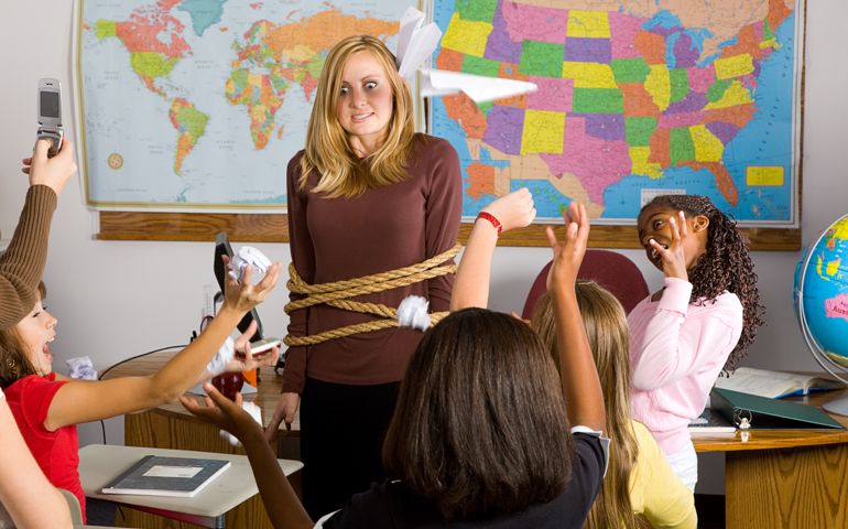 A teacher who is tied up in the middle of an unruly classroom of children.