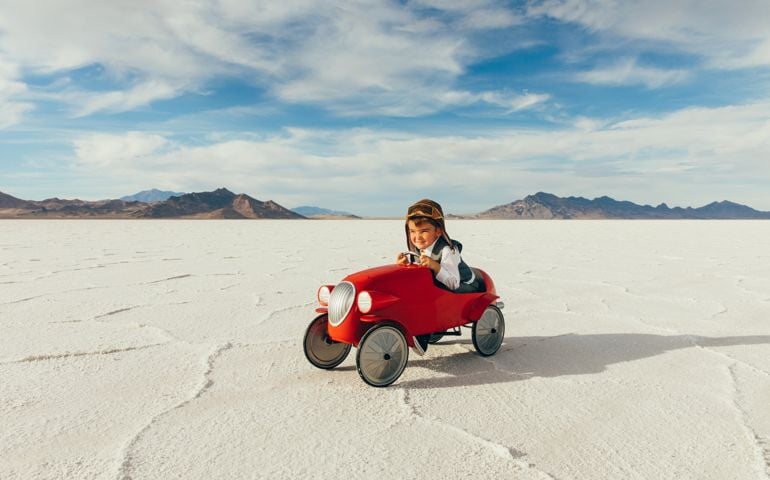 A young boy dressed in a business suit drives his vintage toy car on the salt flats located in Utah, USA. He is excited to race his business into profitability to the next travel destination.