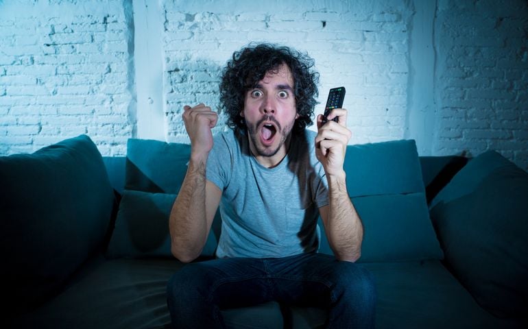 Lifestyle portrait of tv show fan man watching excited favorite series movie or soccer football game in online TV late at night. In people streaming content addiction and entertainment concept.
