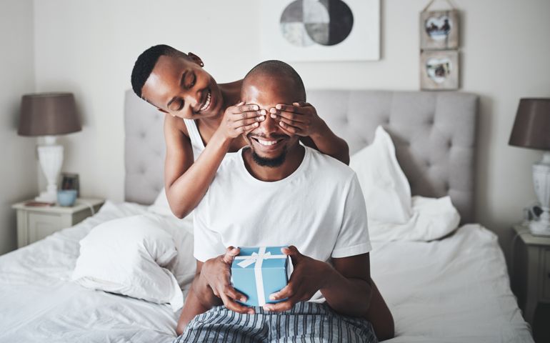 Shot of a young woman surprising her husband with a gift in the bedroom at home