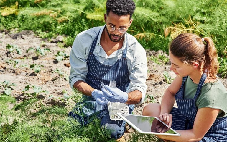Shot of two young botanists using a digital tablet while fertilizing crops and plants outdoors on a farm