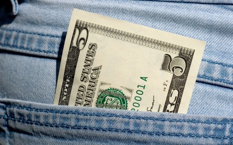Macro of a new US five dollar bill in a jeans pocket.