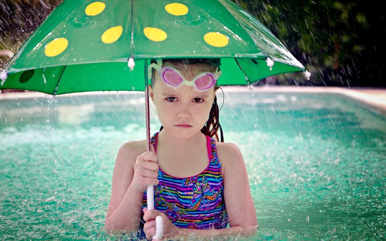 Sad girl holding an umbrella in a pool as it rains