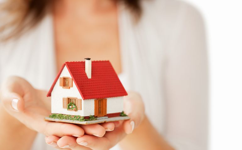 Close-up of woman's hands holding a small model house. Horizontal shot. Isolated on white.
