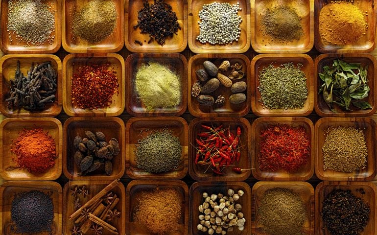 A large selection of commonly used Indian cooking spices in wooden trays on an old table. Spices include, chili ,cumin, tumeric, corriander, cumin, cardamon, garam masala, saffron, cinamon and star anise, poppy seed, sesame, cloves, nutmeg, black and white pepper corns, aniseed and fenugreek.