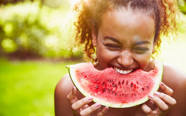 portrait of a young woman eating watermelon on a sunny day, backlit