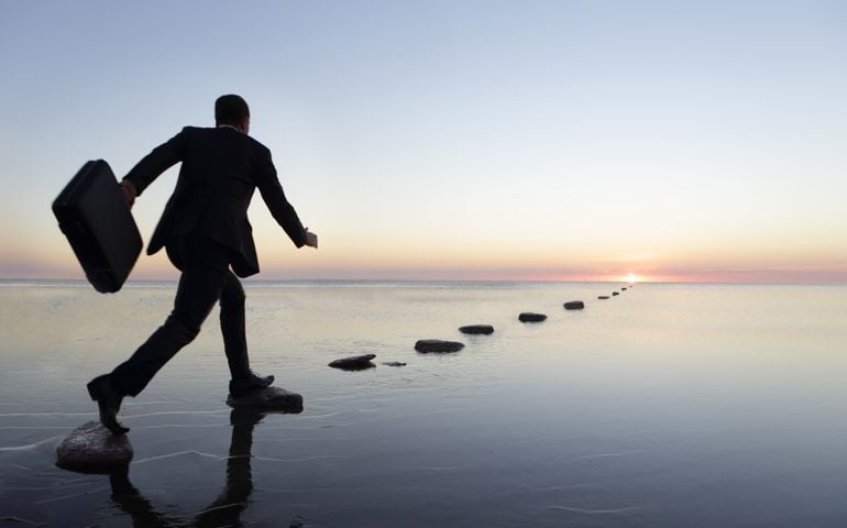 man at sunset in a suit, running over steppingstone