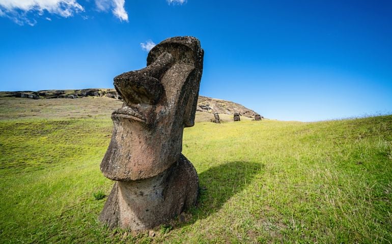Shot of Easter Island Moai Statue at Rano Raraku, on green grass volcanic hills under sunny deep blue summer sky. Rano Raraku, Rapa Nui National Park, Hanga Roa, Easter Island, Chile.