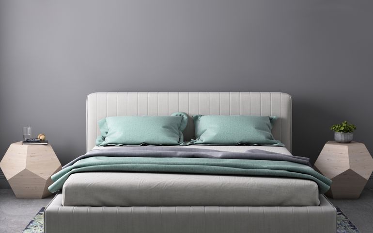 Interior bedroom close up with bed, pastel colored pillows, modern nightstand and wall lamp. Copy space template