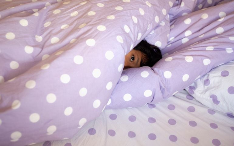 Nine year old girl hides under the polka dotted sheets in bed.